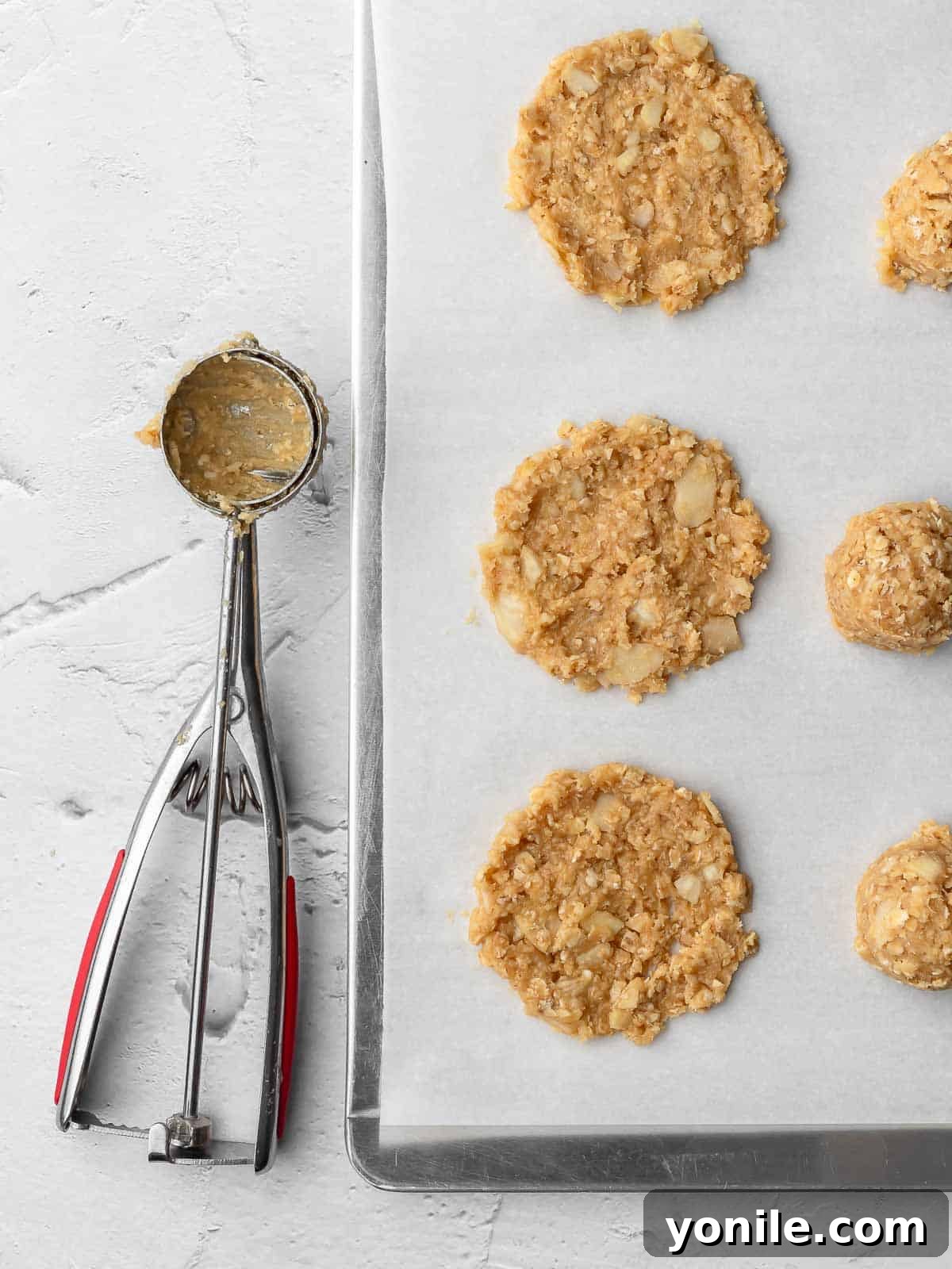 Unbaked crispy almond oatmeal cookie dough portions placed on a parchment-lined baking sheet, ready for the oven.