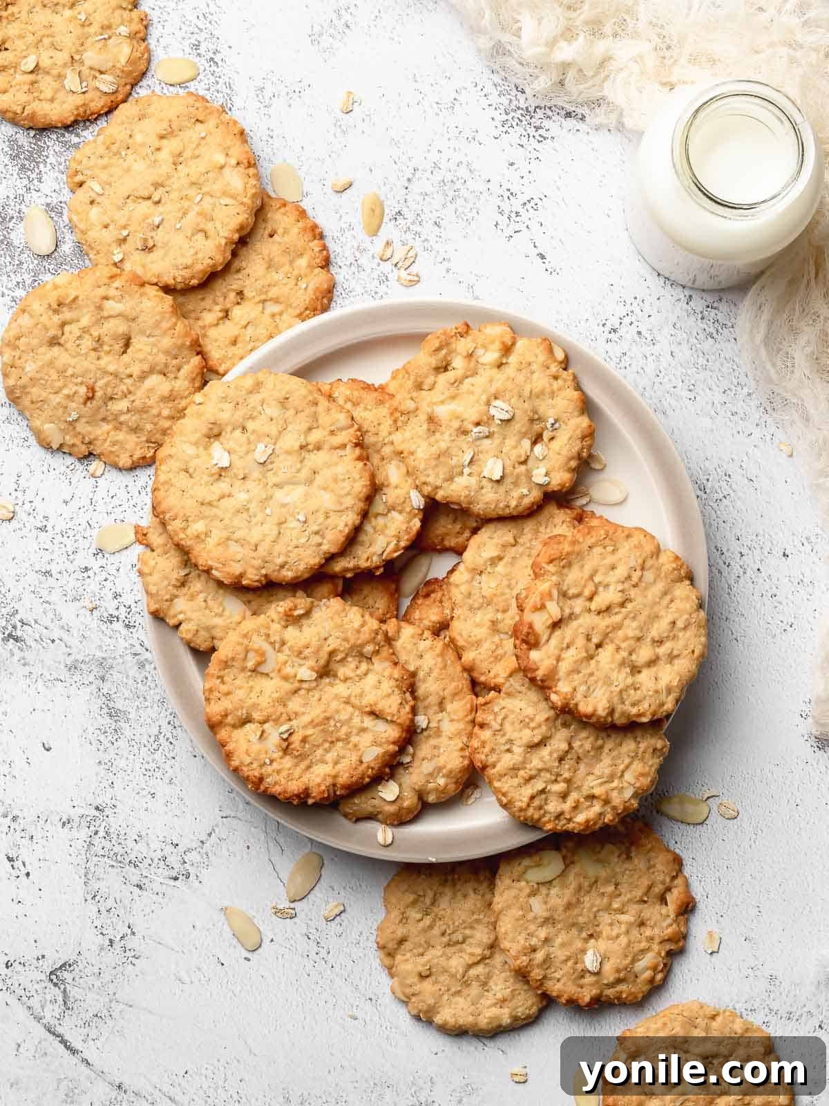 A crispy almond oatmeal cookie on a white plate, accompanied by a glass bottle of milk, suggesting a perfect pairing.