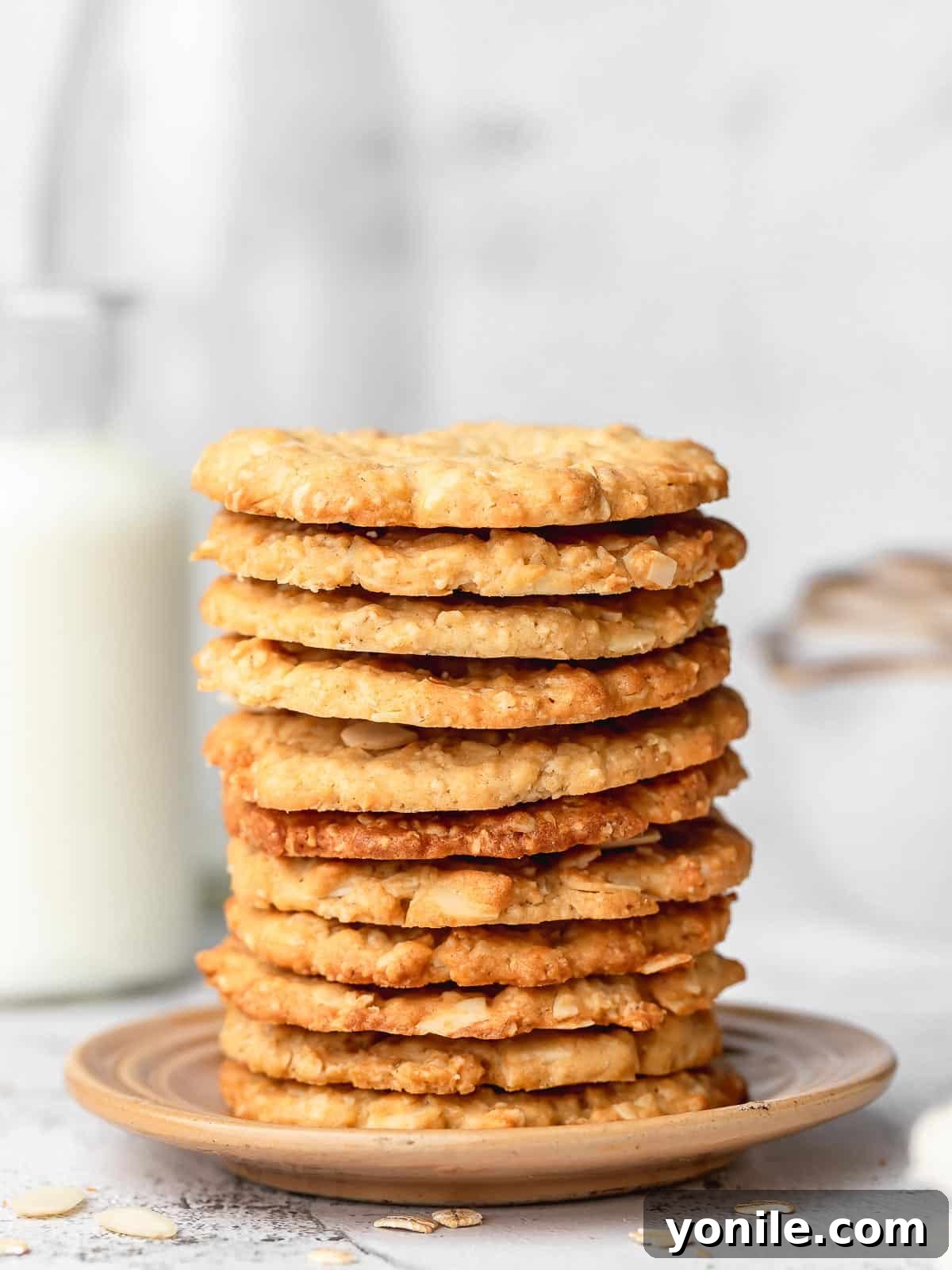 A stack of golden brown crispy almond oatmeal cookies on a small white plate, ready to be enjoyed.
