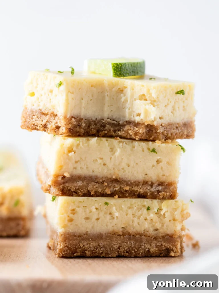 Three golden Key Lime Pie bars stacked on a plate, with one bar showing a bite taken out, revealing the creamy lime filling and the sturdy graham cracker crust.