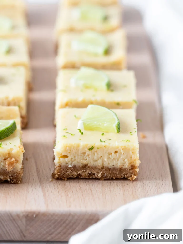 Neatly sliced Key Lime Pie bars arranged on a wooden serving board, showcasing their vibrant green filling and golden crust.