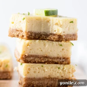 Three golden Key Lime Pie bars stacked on a plate, with one bar showing a bite taken out, revealing the creamy lime filling and the sturdy graham cracker crust.