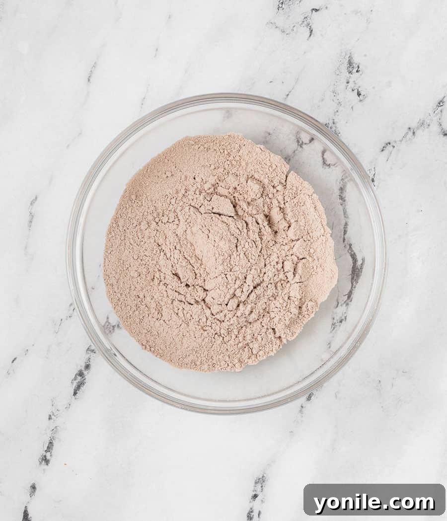 Close-up of dry ingredients – powdered sugar, almond flour, and cocoa powder – perfectly sifted and combined in a bowl, ready for the wet mixture.