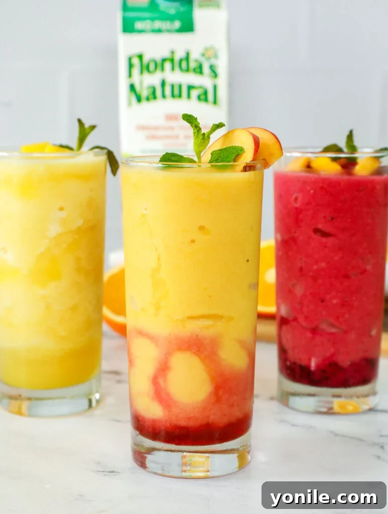 Three glasses of vibrant orange juice slushies, garnished with fresh fruit and mint, arranged beautifully on a table.
