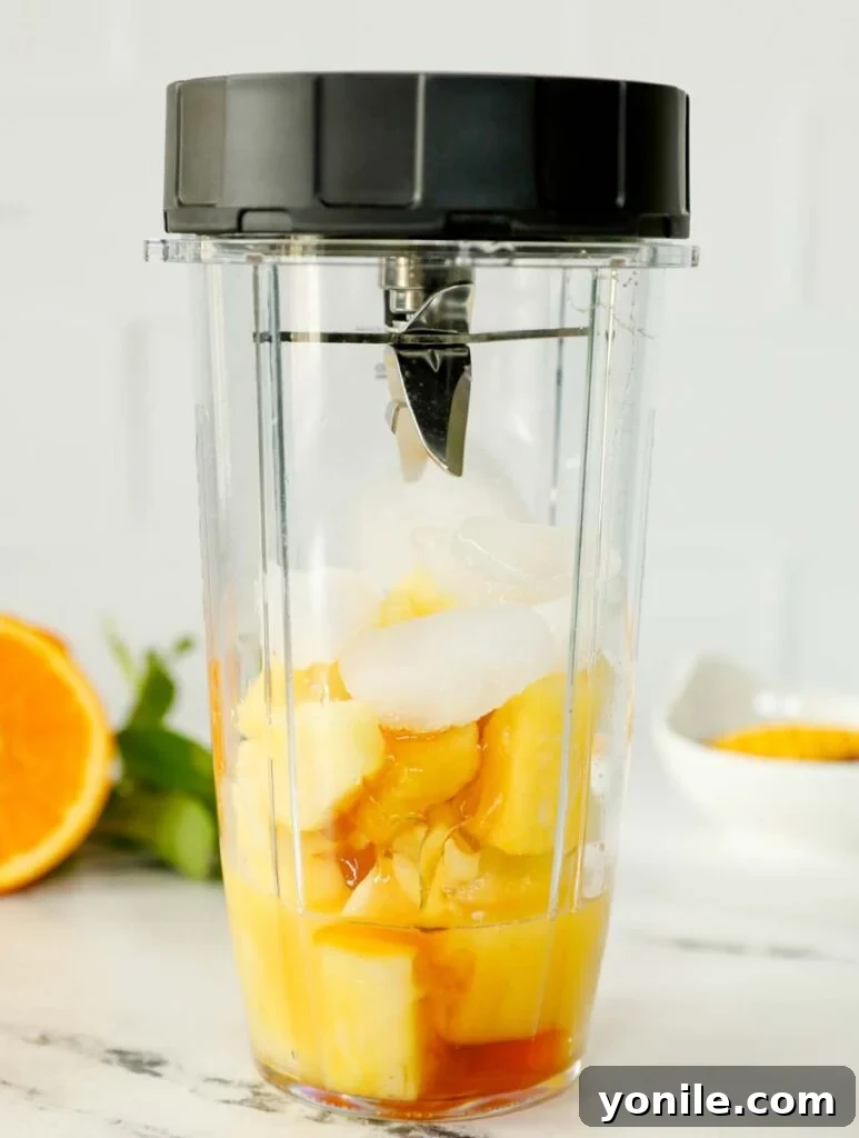 Frozen pineapple chunks and orange juice placed inside a high-speed blender, ready to be blended into a delicious slushie.