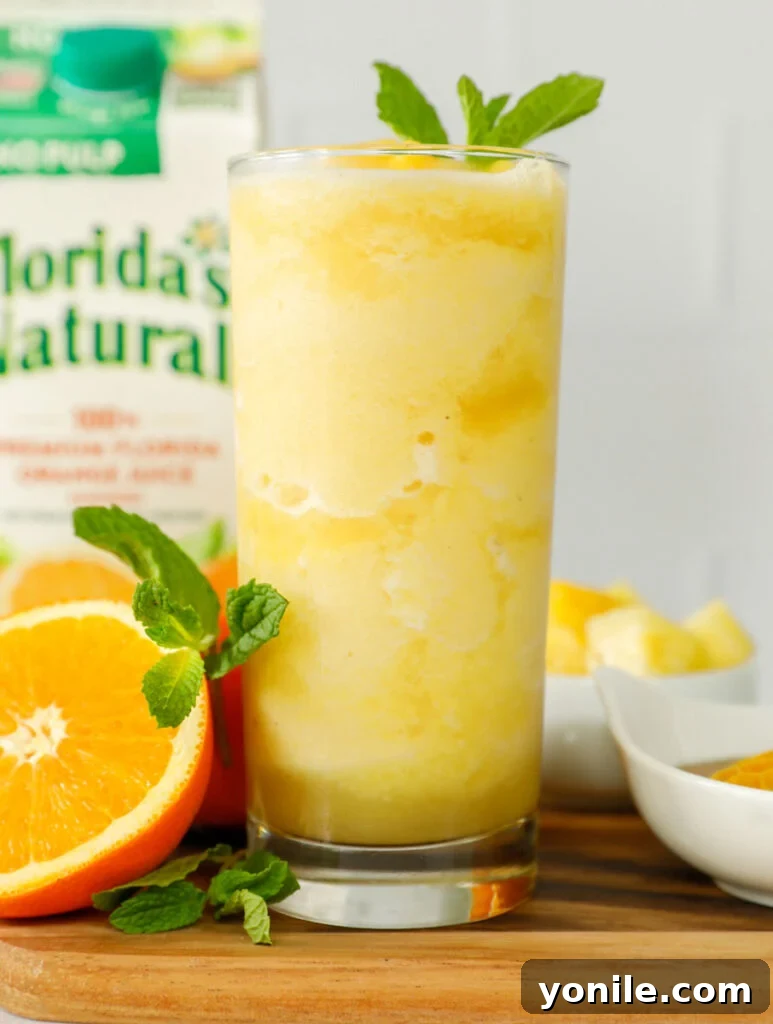 A tall, elegant glass filled with a vibrant pineapple slushie, perfectly blended and garnished with a fresh pineapple wedge.
