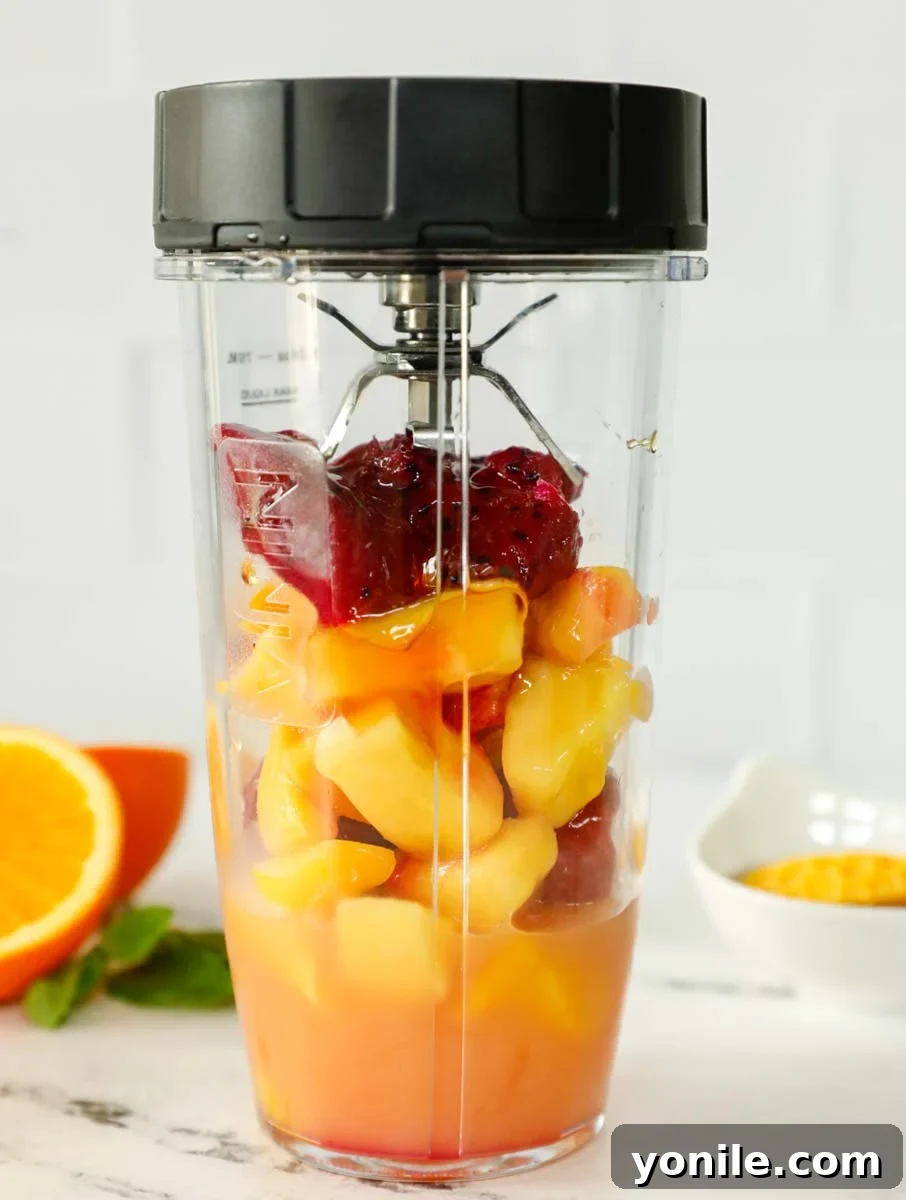 A colorful assortment of tropical smoothie ingredients, including mango, pineapple, and vibrant dragon fruit, nestled inside a blender, ready for blending.