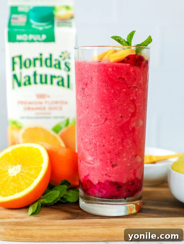 A tall glass filled with a vibrant tropical smoothie, made with orange juice and garnished with a selection of fresh exotic fruits.