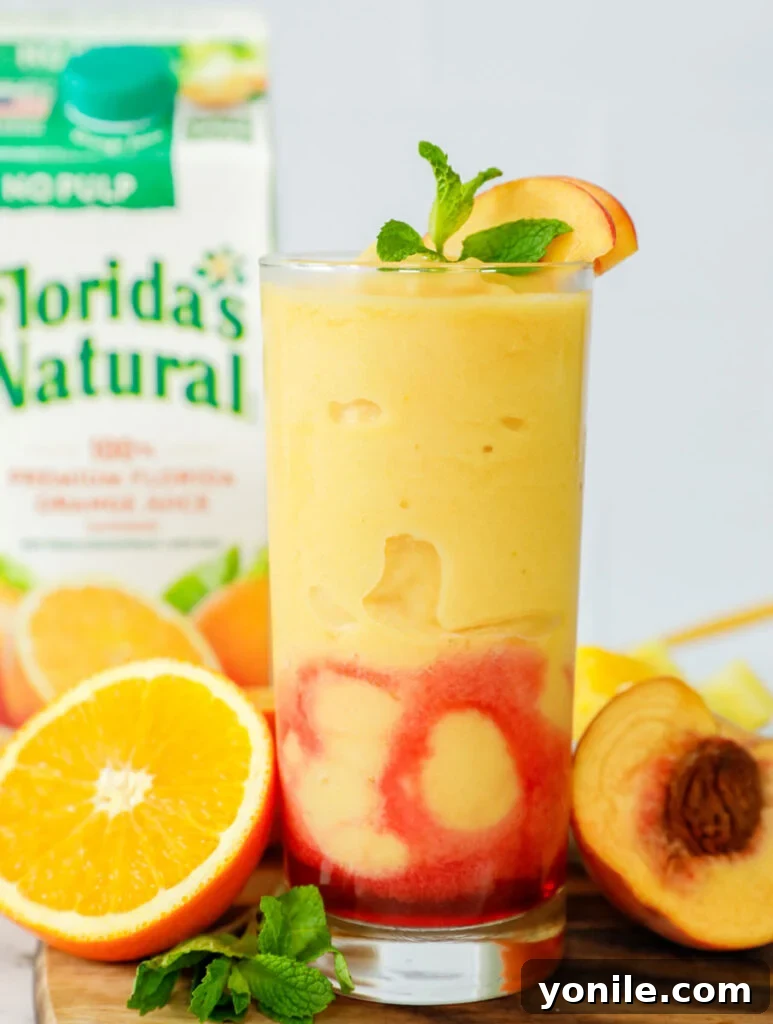A tall glass of the Peach N' Orange slushie, beautifully garnished with fresh peach slices and a mint sprig.