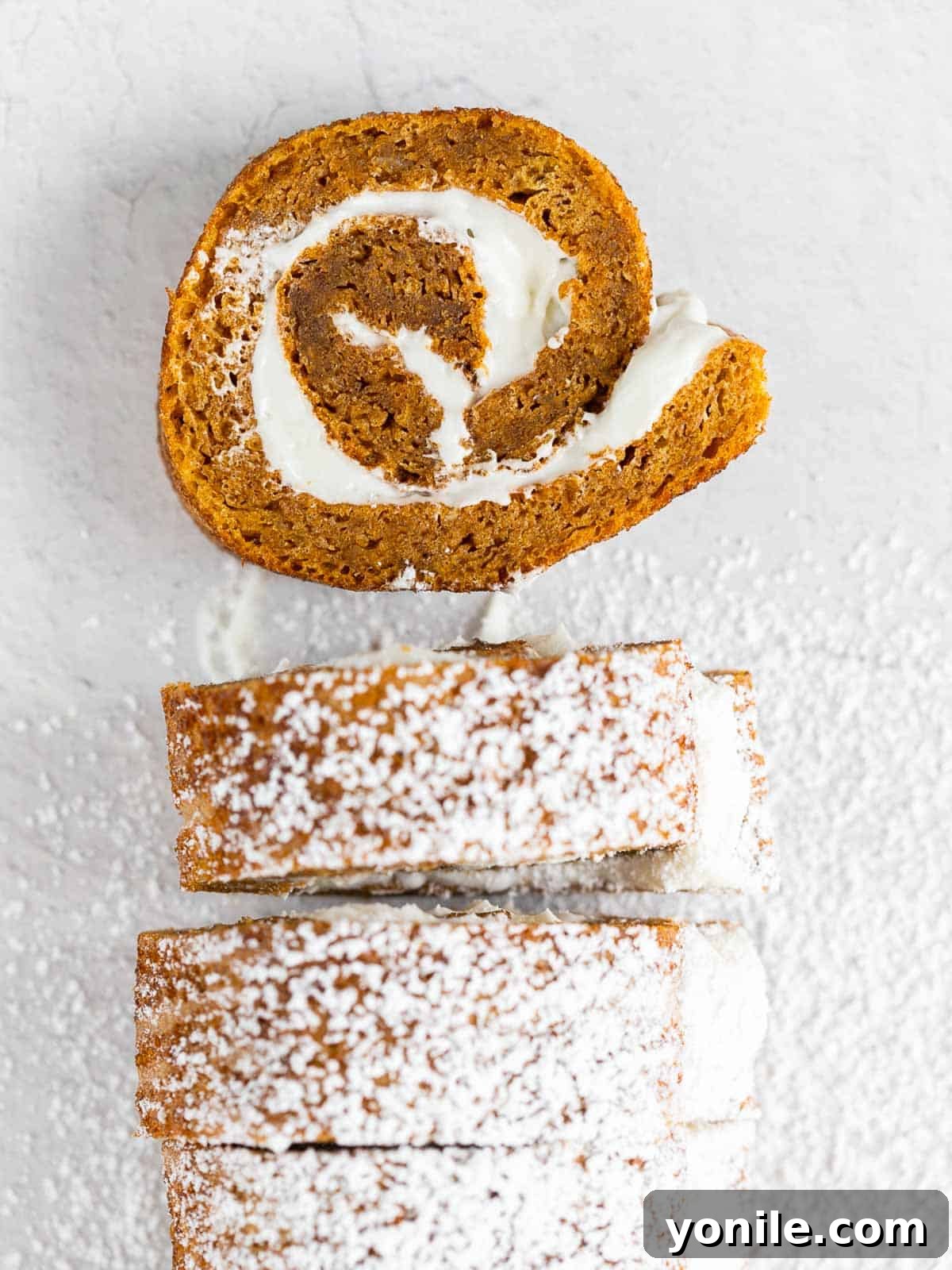 Slices of fluffy pumpkin cake roll generously dusted with powdered sugar, ready to be served on a pristine white plate.