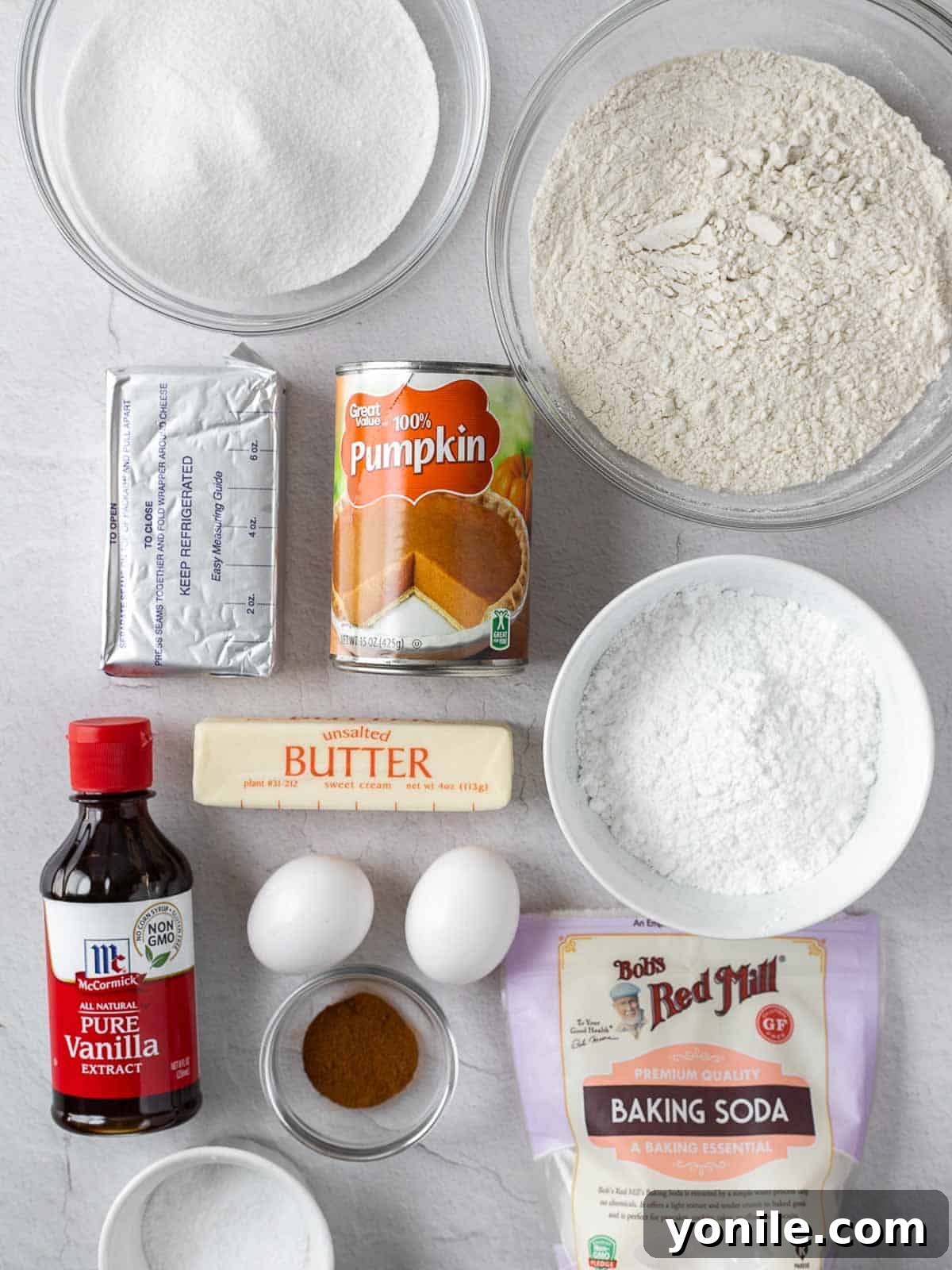 A selection of fresh ingredients laid out on a kitchen counter, including flour, baking soda, pumpkin spice, sugar, eggs, vanilla extract, and a can of pumpkin puree, all ready for baking a pumpkin cake roll.