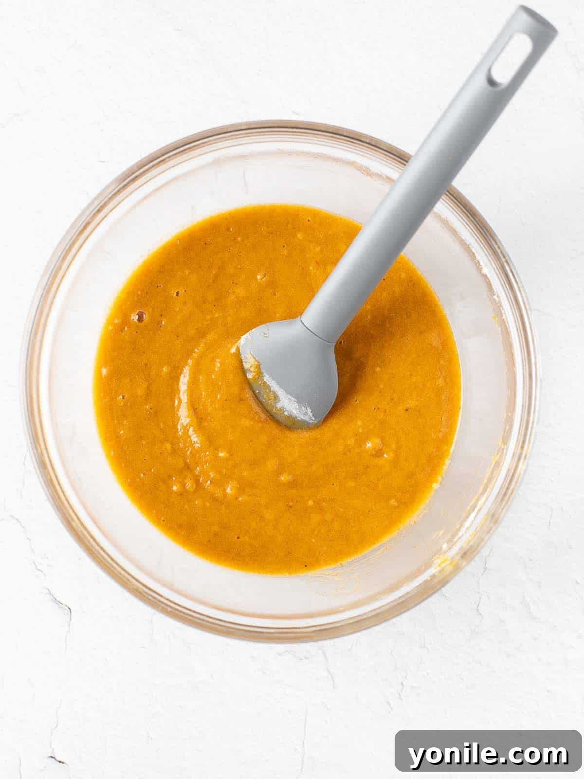 Smooth, orange-hued pumpkin cake batter expertly prepared in a large mixing bowl, ready to be poured into the baking pan.