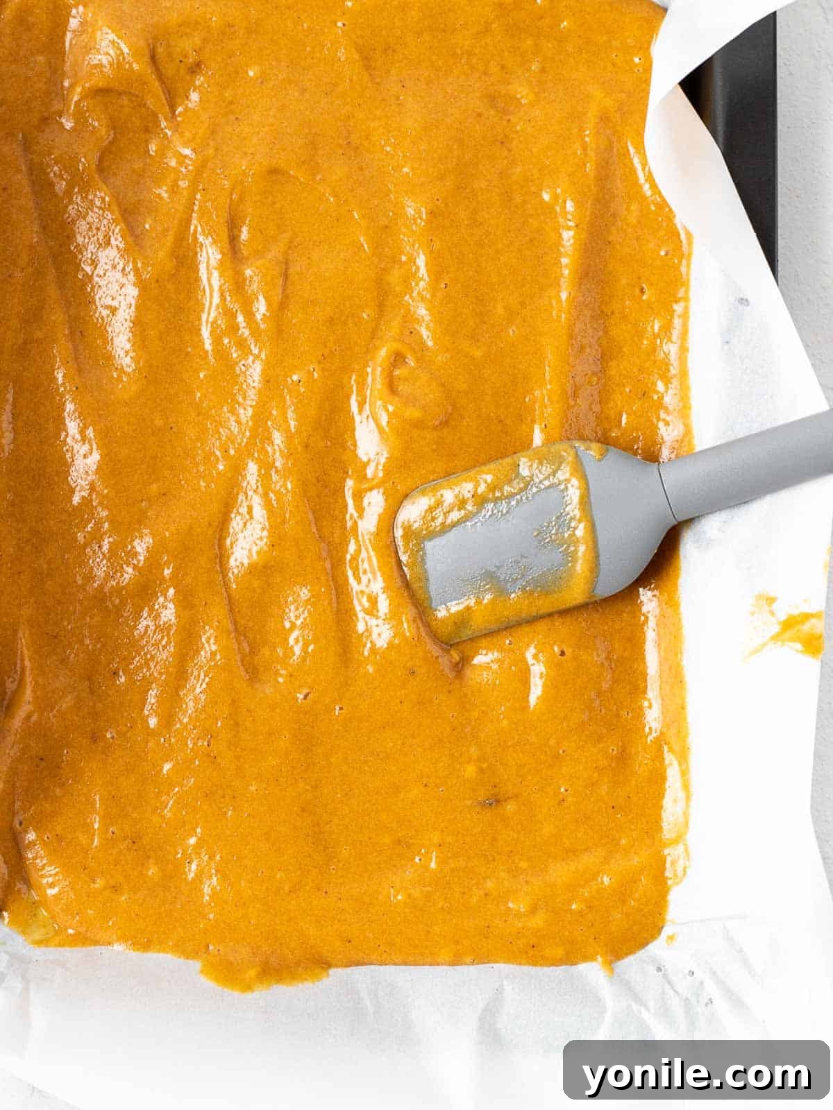 Golden-orange pumpkin cake batter smoothly and evenly spread across a parchment-lined baking pan, poised for baking.