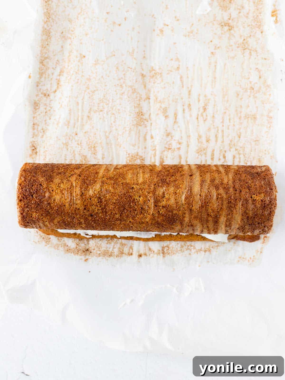 A freshly baked pumpkin cake, still warm, carefully rolled into a tight log with its parchment paper, cooling on a wire rack.