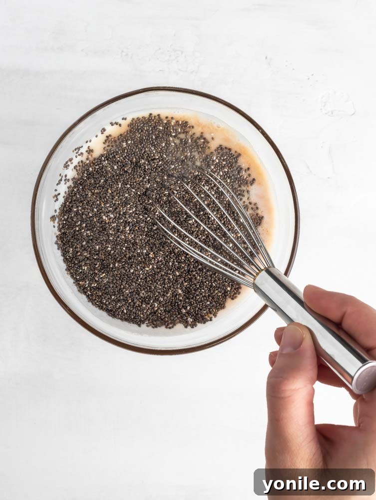 Velvet Chocolate Chia Morning 4 A person mixing chia seeds and almond milk in a bowl with a whisk.