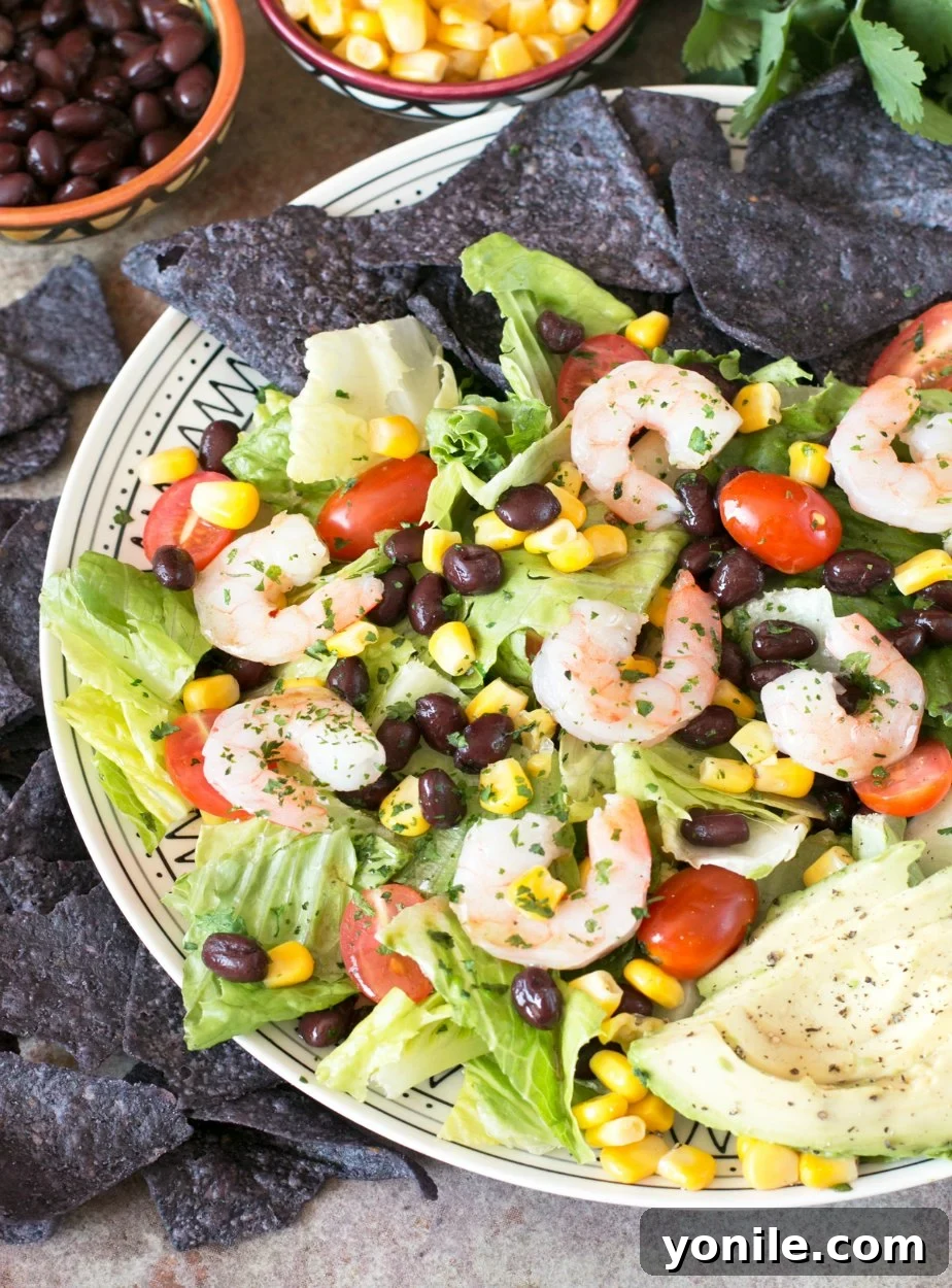 A vibrant Mexican Shrimp Taco Salad served on a pristine white plate, accompanied by a scattering of blue corn tortilla chips for a delightful crunch.