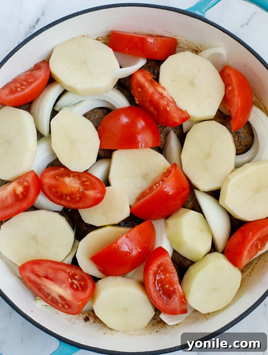 Lebanese Kofta Stew for Beginners 9 A close-up view of kafta patties, sliced potatoes, tomatoes, and onions neatly arranged in a deep pot, ready for simmering.