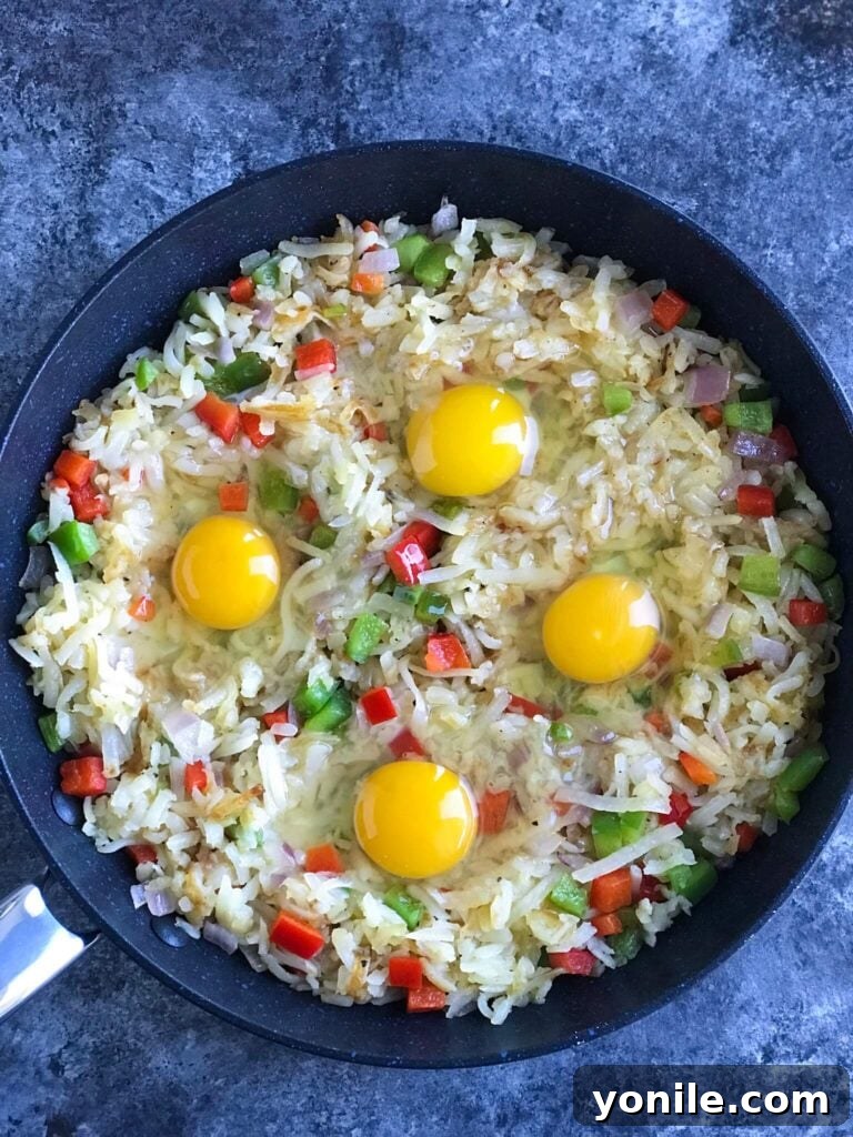 Eggs Cracking into Veggie Hashbrown Skillet