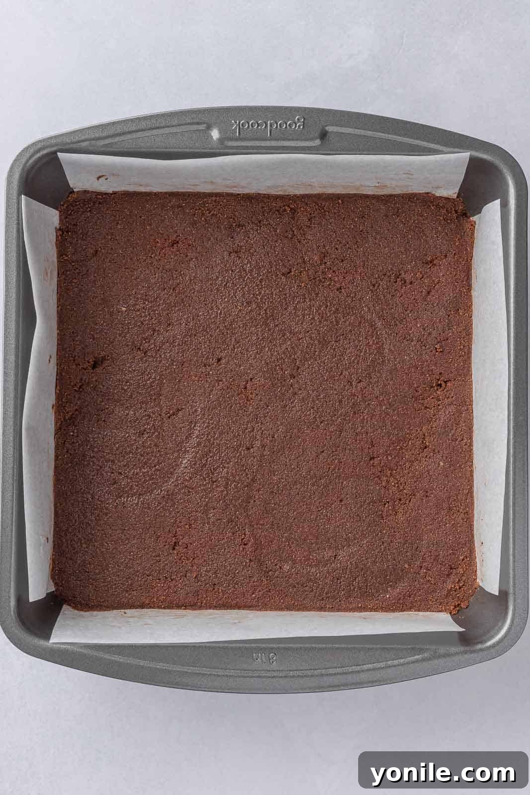 The chocolate graham cracker crust pressed firmly into the bottom of a parchment-lined 8x8 inch baking pan.