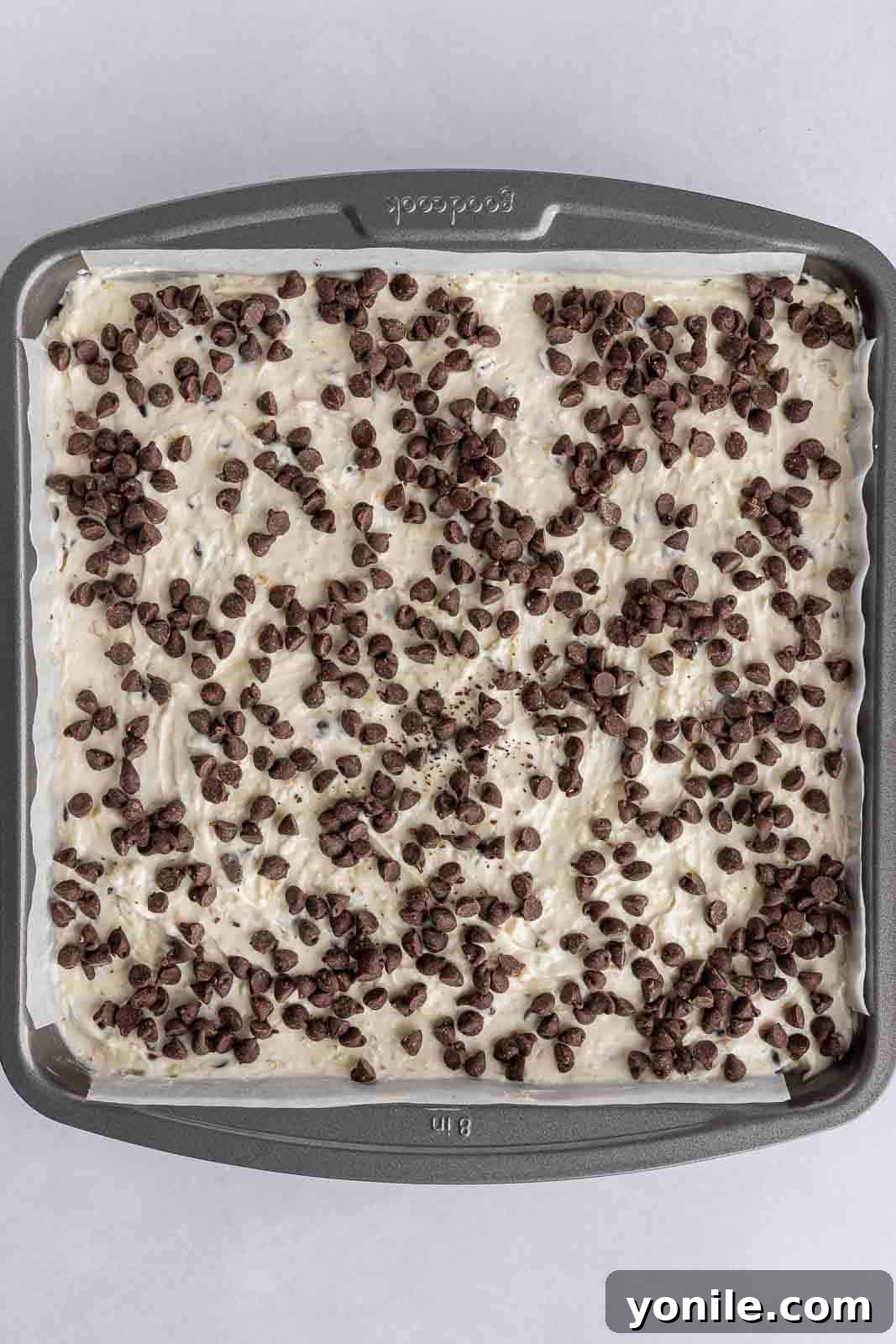 Unbaked Almond Joy cheesecake bars in a pan, topped with chocolate chips, ready for the oven.