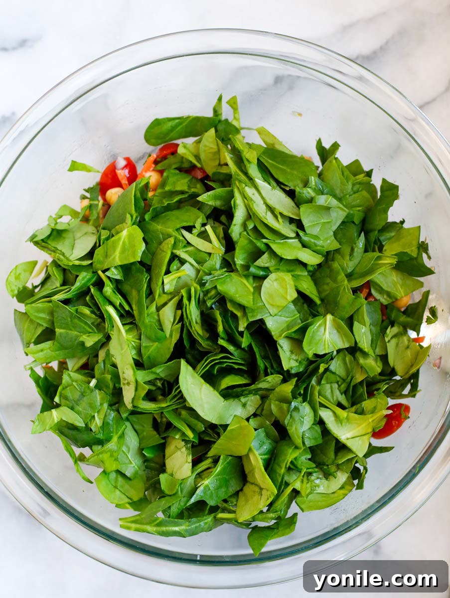 Fresh baby spinach leaves being added to a large bowl of other salad ingredients.