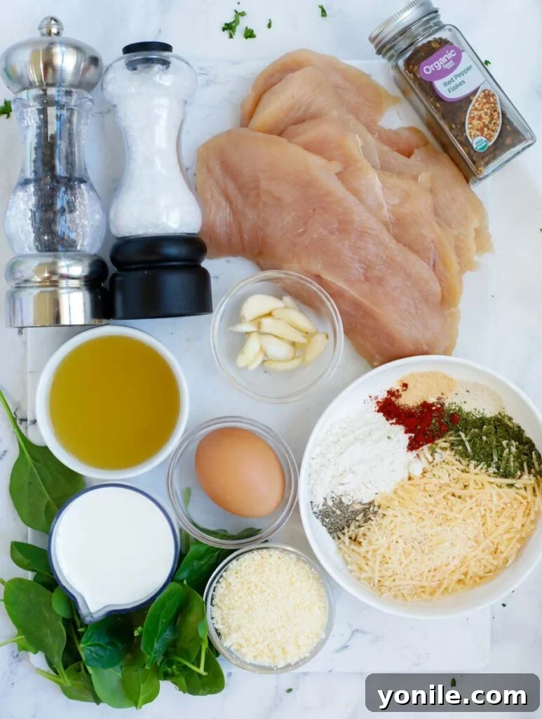 Arrangement of fresh ingredients including chicken breasts, parmesan, spinach, and spices, laid out for creamy parmesan chicken.