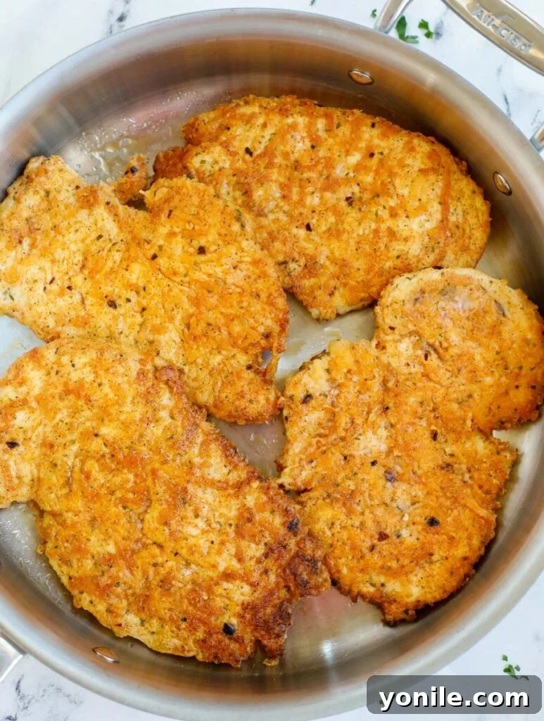 Crispy, golden-brown pan-seared chicken breasts cooking in a skillet.