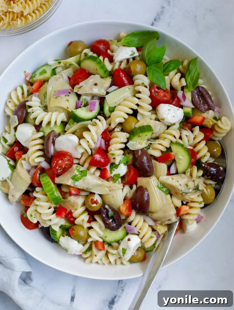 Vibrant Mediterranean Pasta Medley 9 A close-up shot of a bowl of Mediterranean pasta salad with a serving spoon, presented on a marble surface.