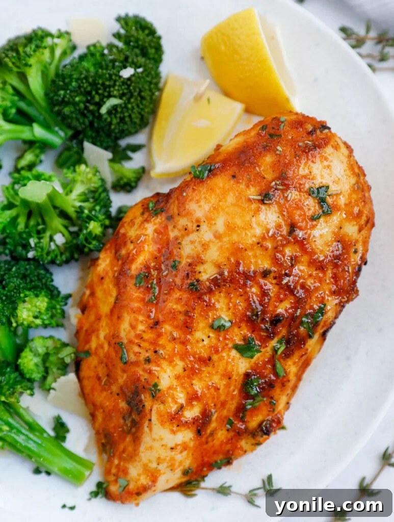 Crispy Rosemary Air Fryer Chicken 2 Close up of an air fryer rosemary chicken breast beside some broccoli and lemon wedges.