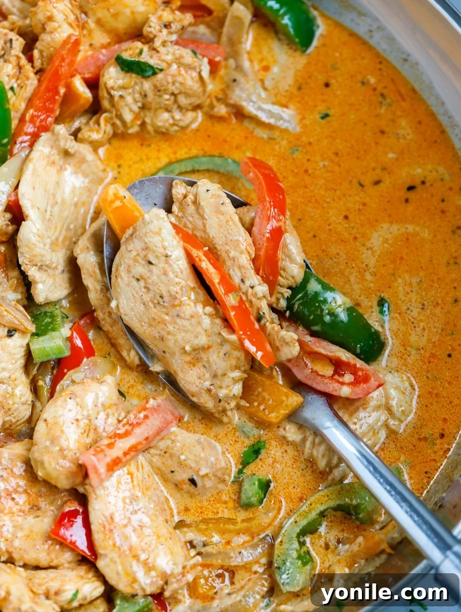 Close up of creamy chicken fajita skillet being served with a spoon, highlighting the rich sauce and tender chicken and vegetables.