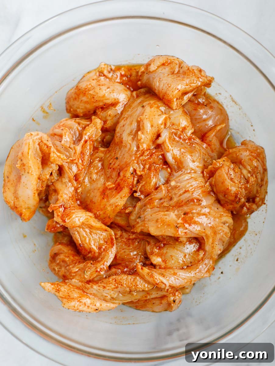 Chicken strips being marinated with spices in a bowl.