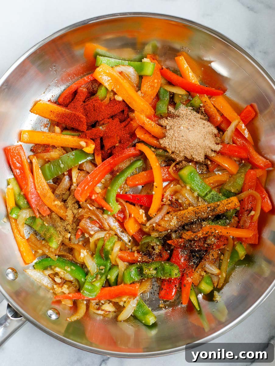 Fajita seasoning and other spices being added to a skillet of sautéed vegetables.
