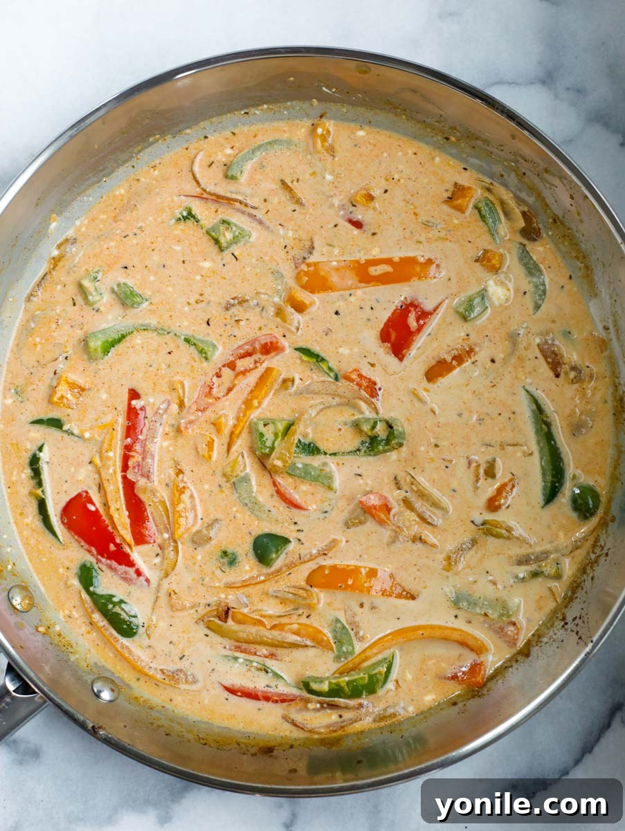 Creamy sauce forming and simmering in the skillet with sautéed vegetables.