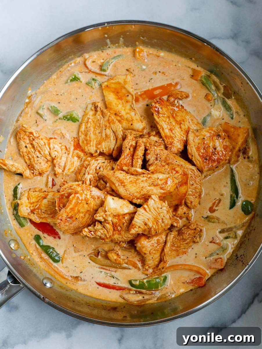 Cooked chicken strips being added back into the skillet with creamy fajita sauce and vegetables.