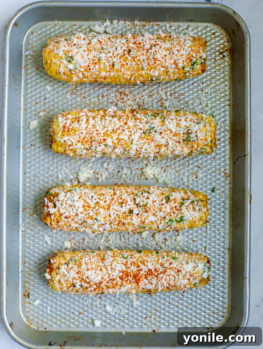 Finished Mexican corn on a sheet pan, garnished with Tajín seasoning and fresh herbs.