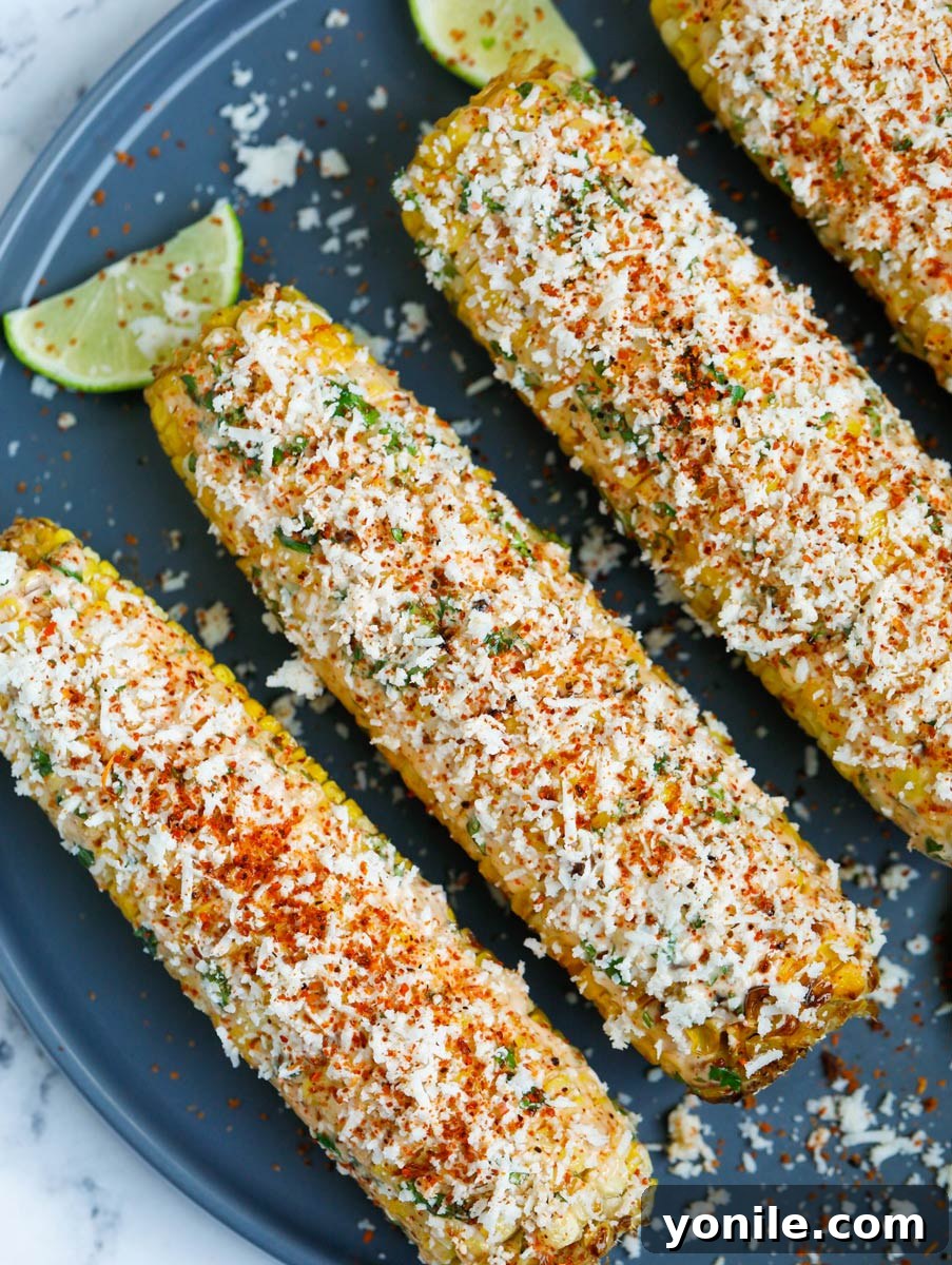 Close-up of a loaded Mexican street corn on a plate, showcasing abundant cheese and sauce.
