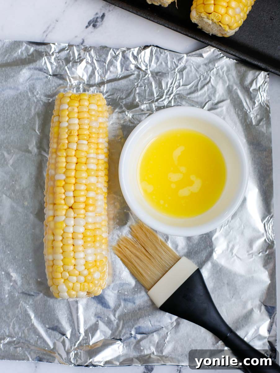 Melted butter being brushed onto a corn on the cob before grilling.