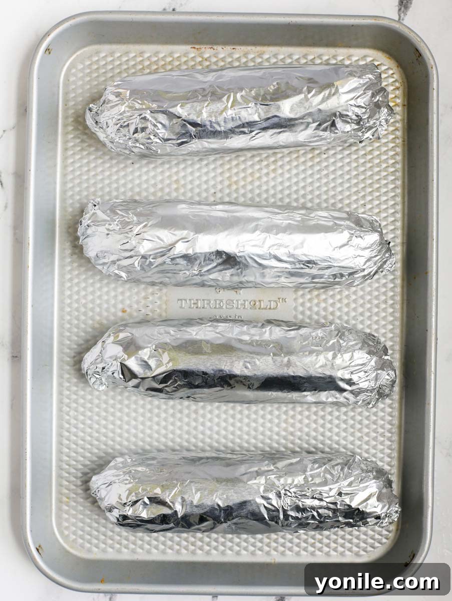 Corn on the cob wrapped individually in aluminum foil, ready for grilling.