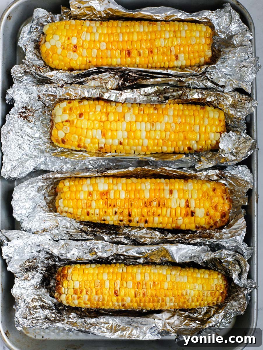 Tin foil wrapped corn grilling on a barbecue, showing light charring through the foil.