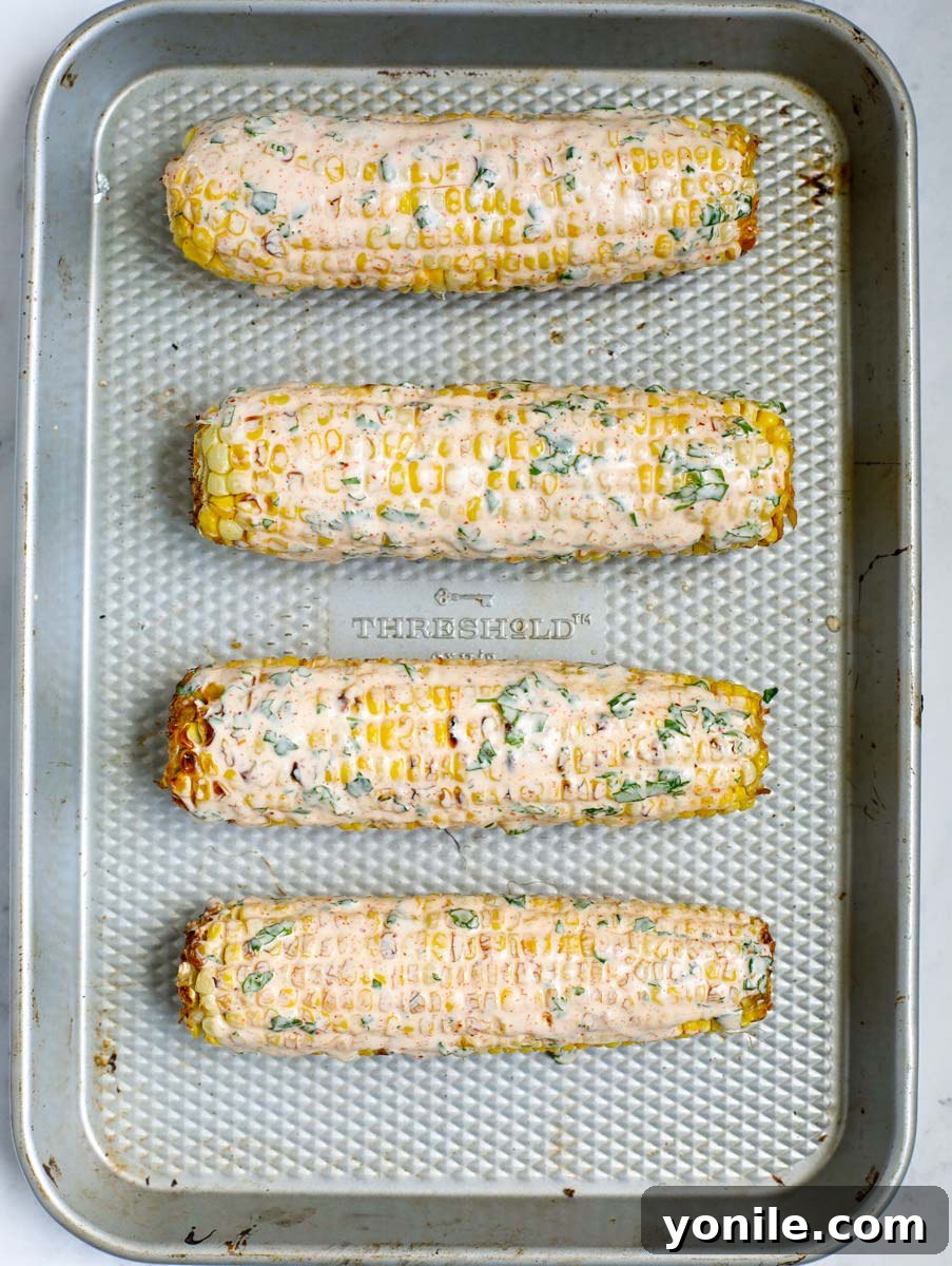 Grilled Mexican street corn being brushed with the creamy Elote sauce.
