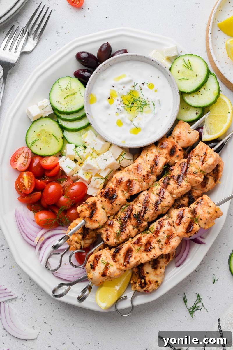 Top-down shot of perfectly grilled Greek chicken skewers served with fresh sides like a vibrant salad and pita bread
