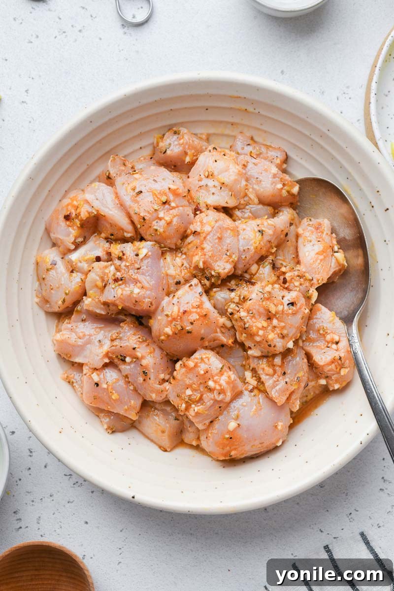 Close-up shot of cubed chicken tenderloins soaking in a vibrant Greek marinade in a mixing bowl