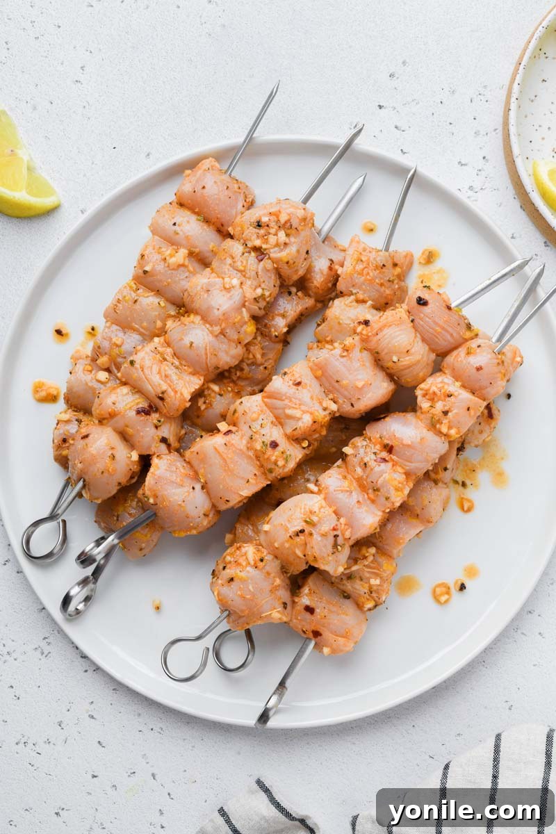 Uncooked marinated Greek chicken threaded onto skewers, ready for grilling, displayed on a plate