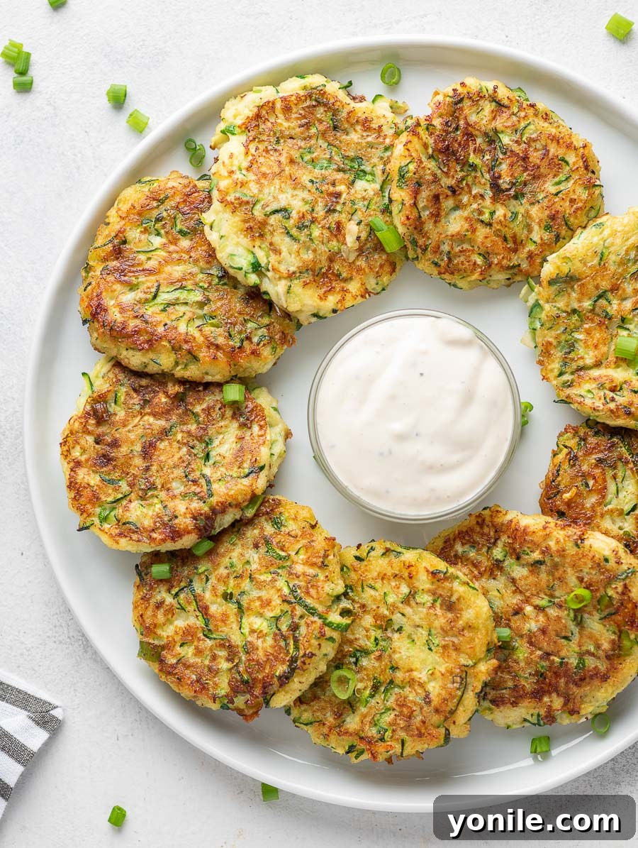 Crispy Zucchini Bites 2 Crispy zucchini fritters served on a white plate with a side of creamy dipping sauce.