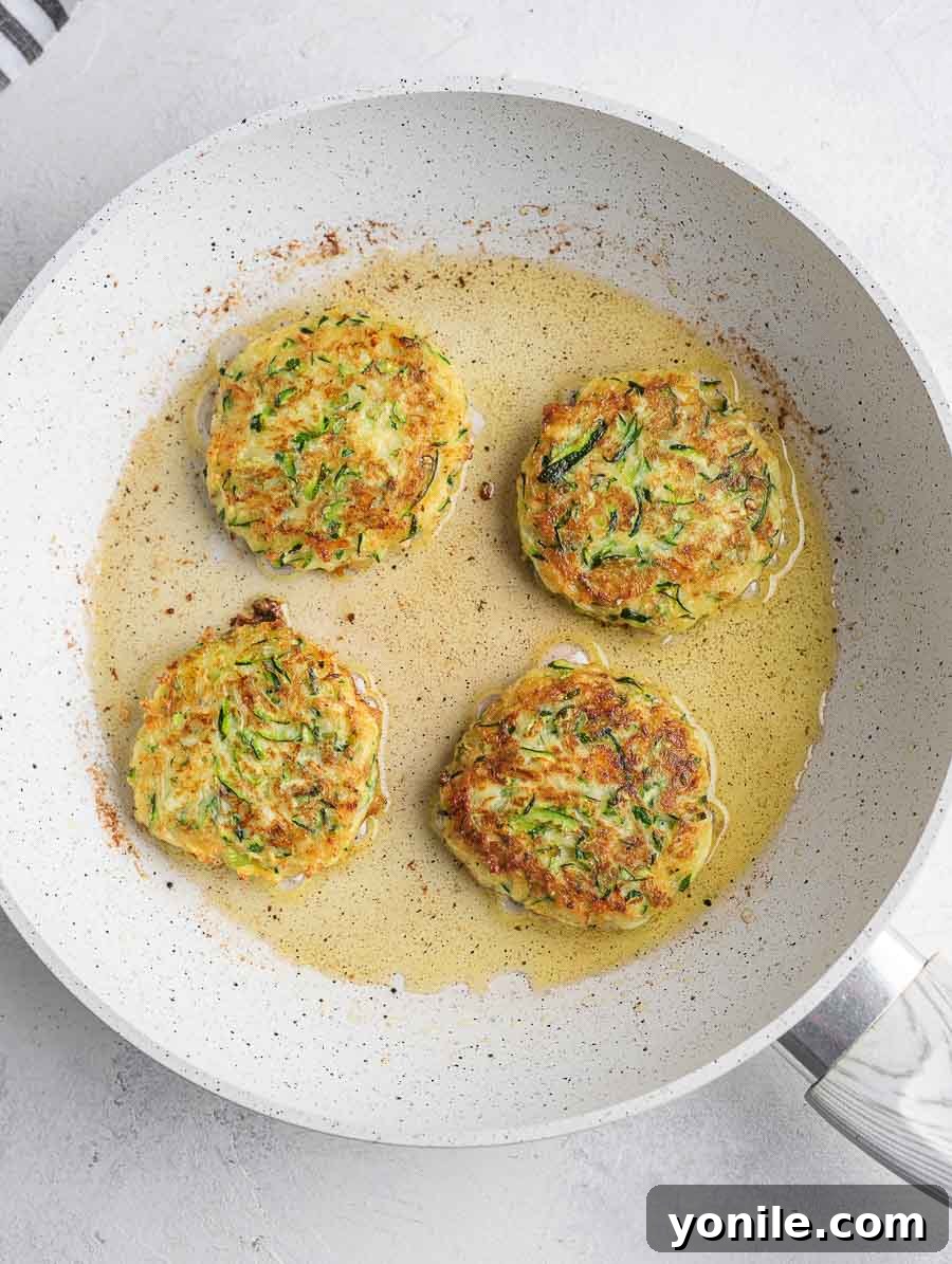 Crispy Zucchini Bites 7 Several zucchini fritters sizzling and turning golden brown in a hot frying pan.