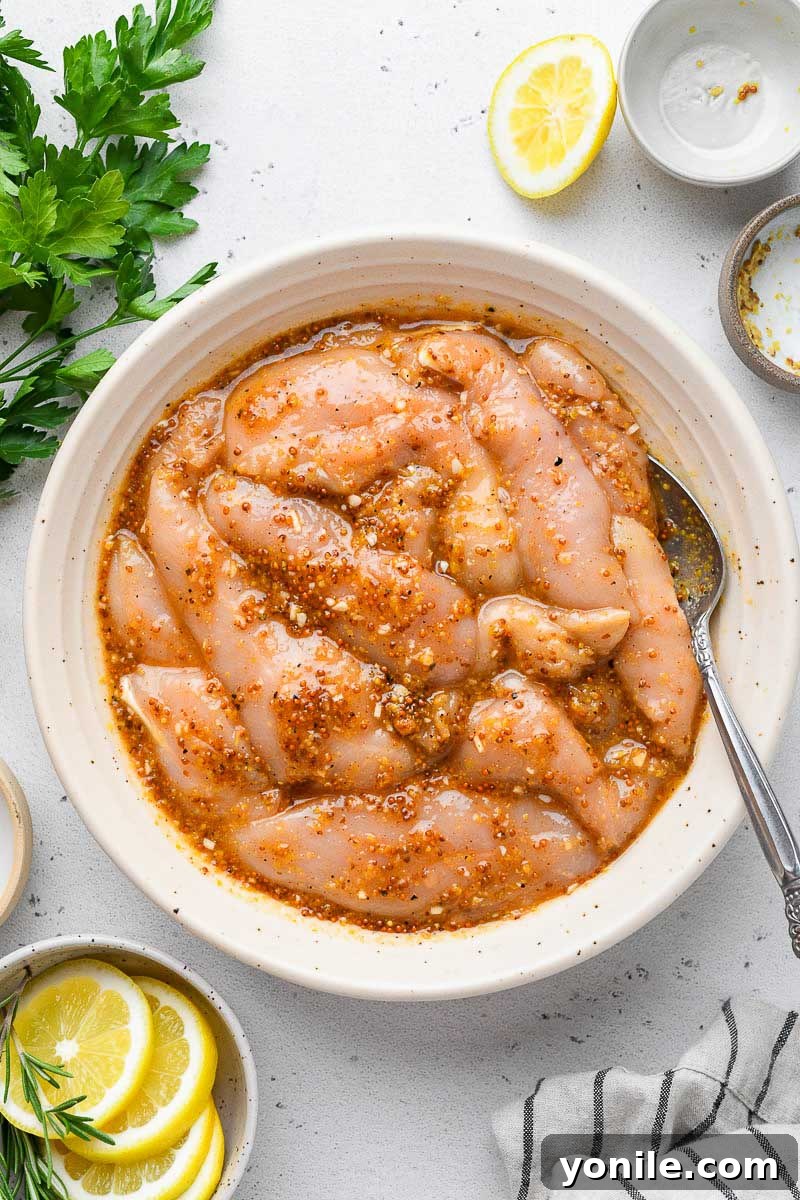 A bowl of raw chicken tenders fully coated and marinaded in honey mustard sauce.