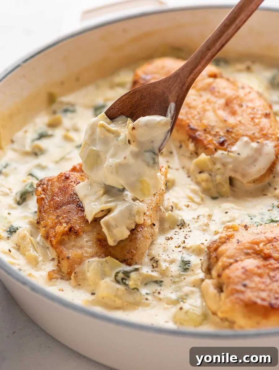 creamy spinach artichoke sauce being placed on top of the chicken