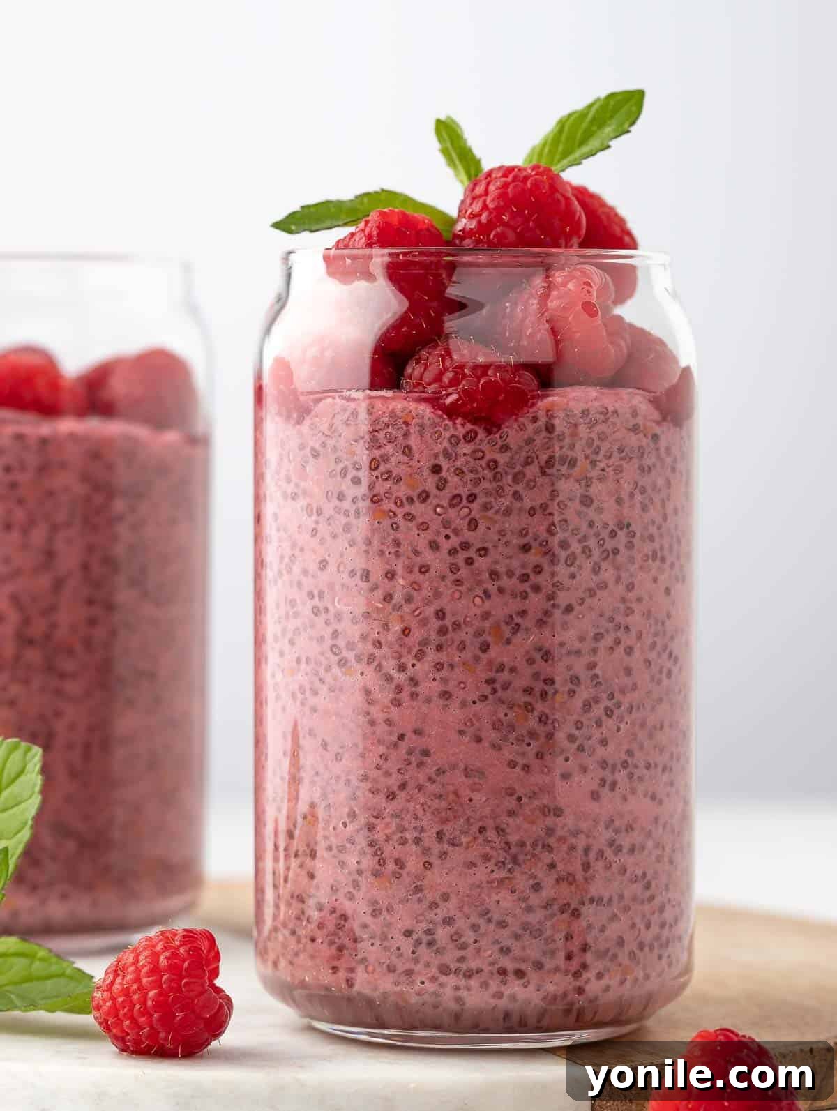 Close up shot of Raspberry Protein Chia Seed Pudding, topped with fresh raspberries and a mint leaf, served in a glass jar.