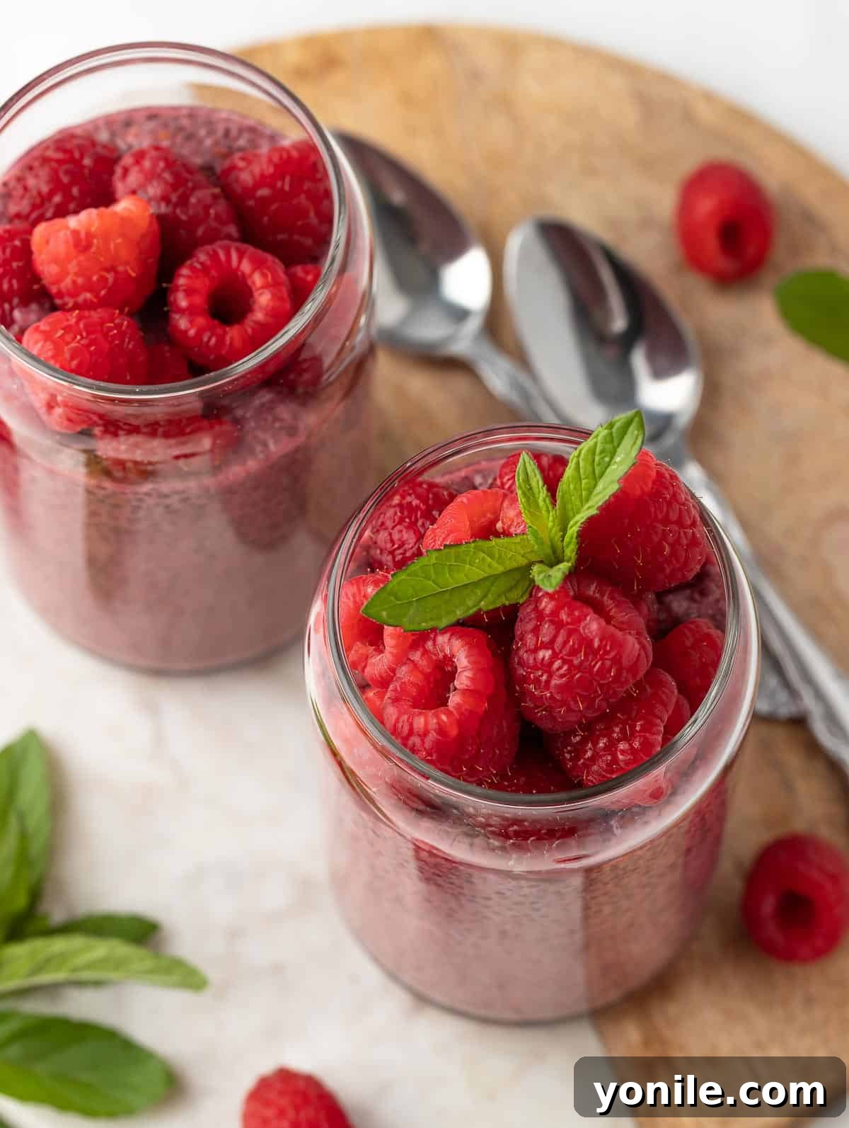 Top shot of Raspberry Protein Chia Seed Pudding, beautifully topped with fresh raspberries and a mint leaf, served with two spoons on a side, highlighting its readiness to be enjoyed.