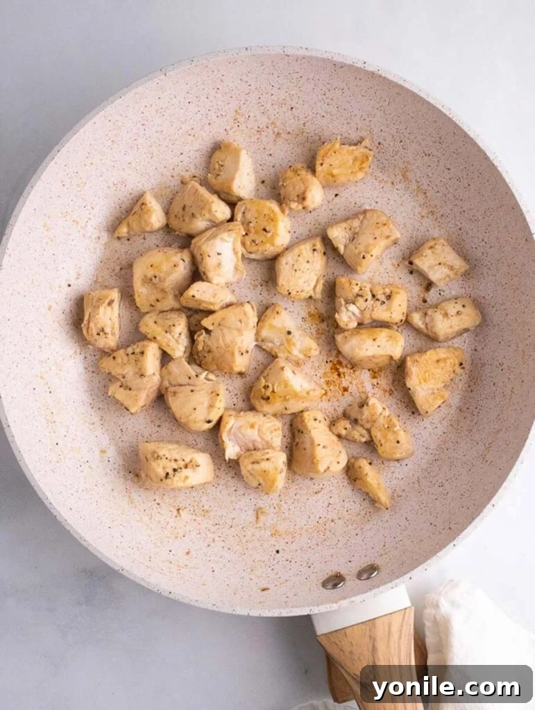 Cooked chicken cubes sizzling in a skillet, browned to perfection.